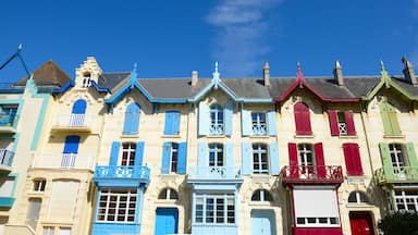 A row of colorful buildings with blue, red, and green shutters under a clear blue sky.