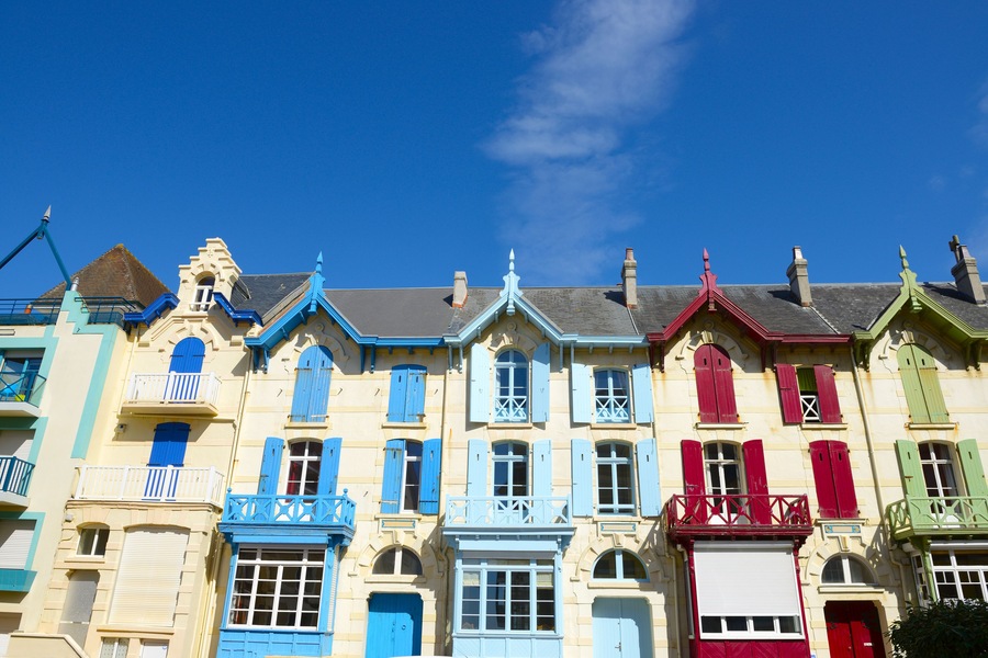 Une rangée de bâtiments aux couleurs vives, avec des volets bleus, rouges et verts, sous un ciel bleu dégagé.