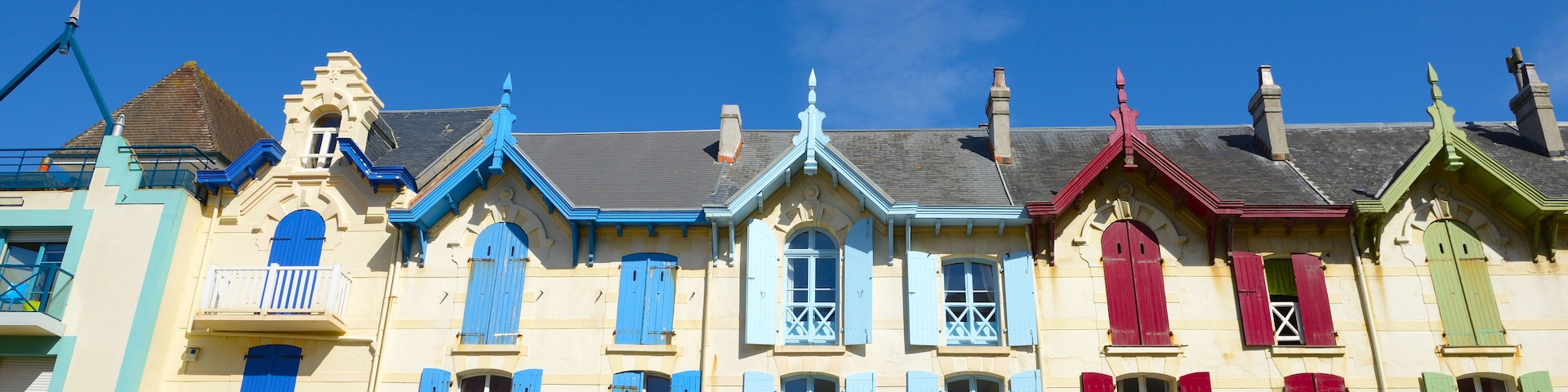 Una hilera de edificios coloridos con contraventanas azules, rojas y verdes bajo un cielo azul despejado.