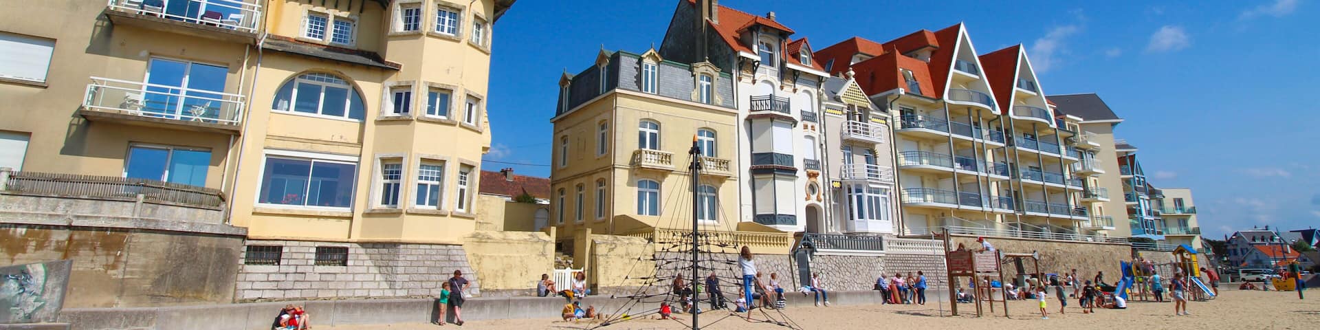 A sandy beach with people, a playground, and multi-story buildings with balconies.