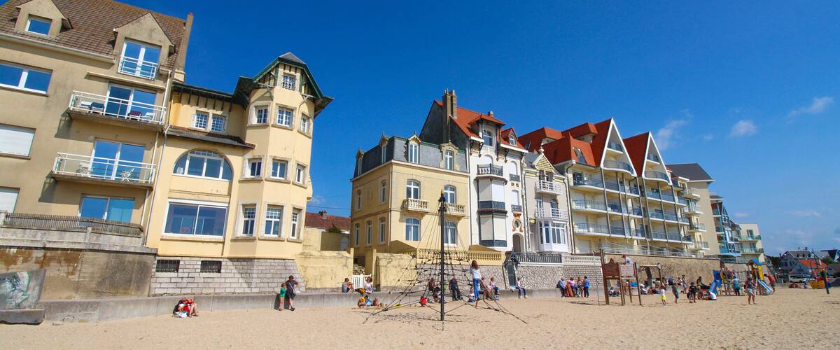 A sandy beach with people, a playground, and multi-story buildings with balconies.