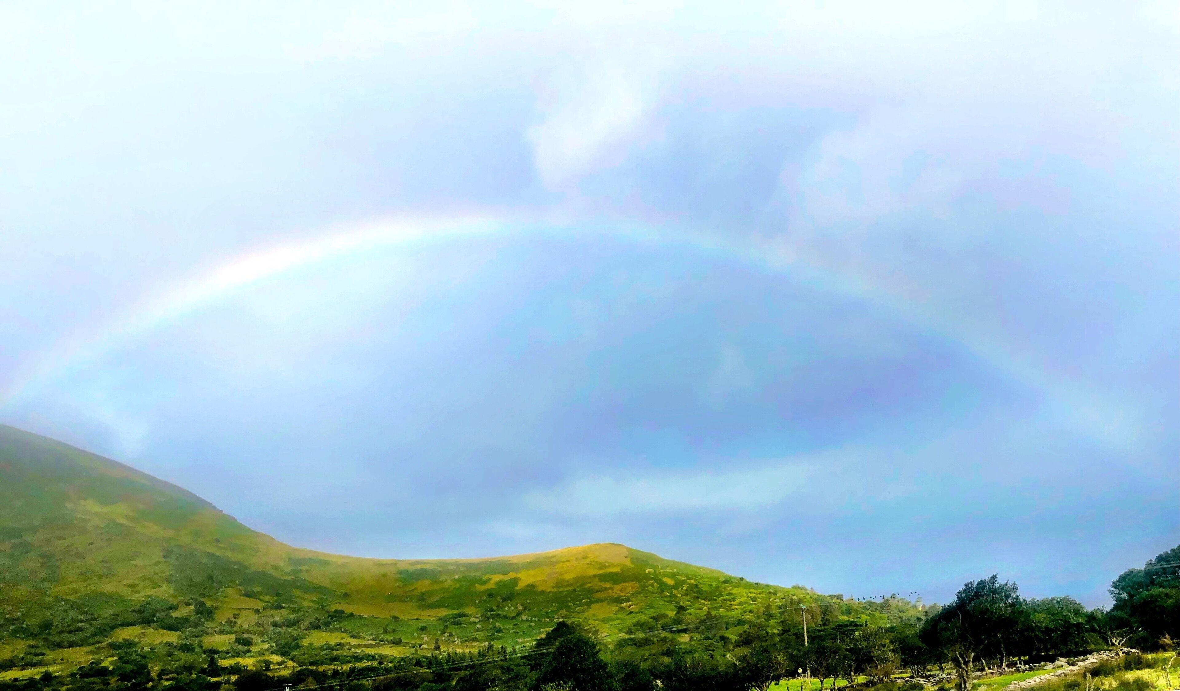 A landscape with a rainbow over rolling hills and a clear sky.