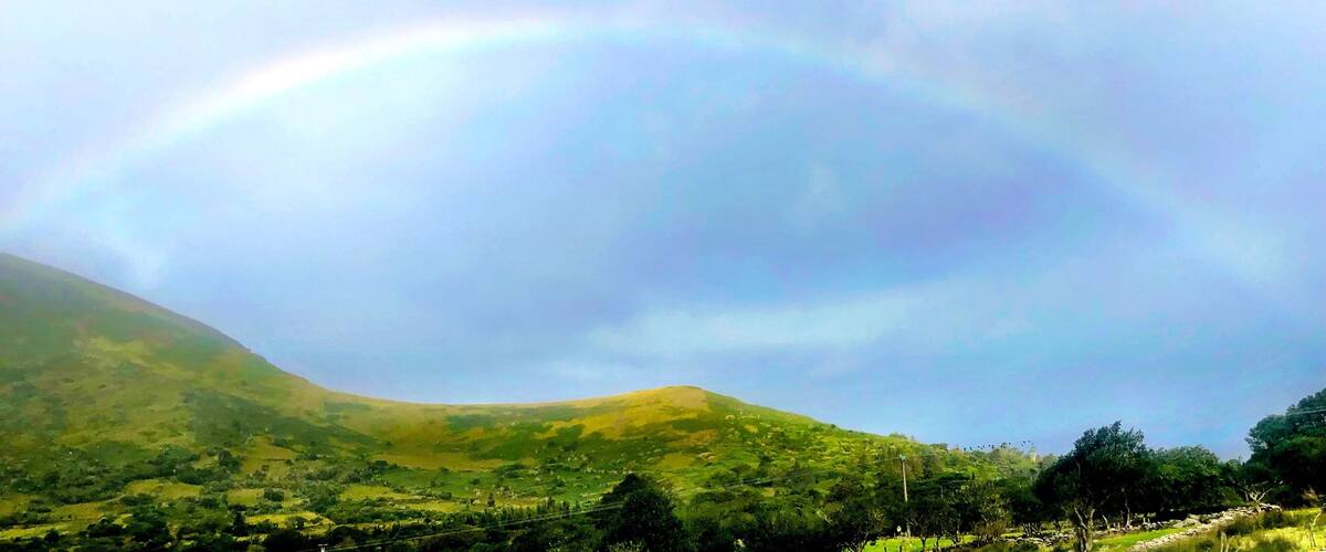A landscape with a rainbow over rolling hills and a clear sky.