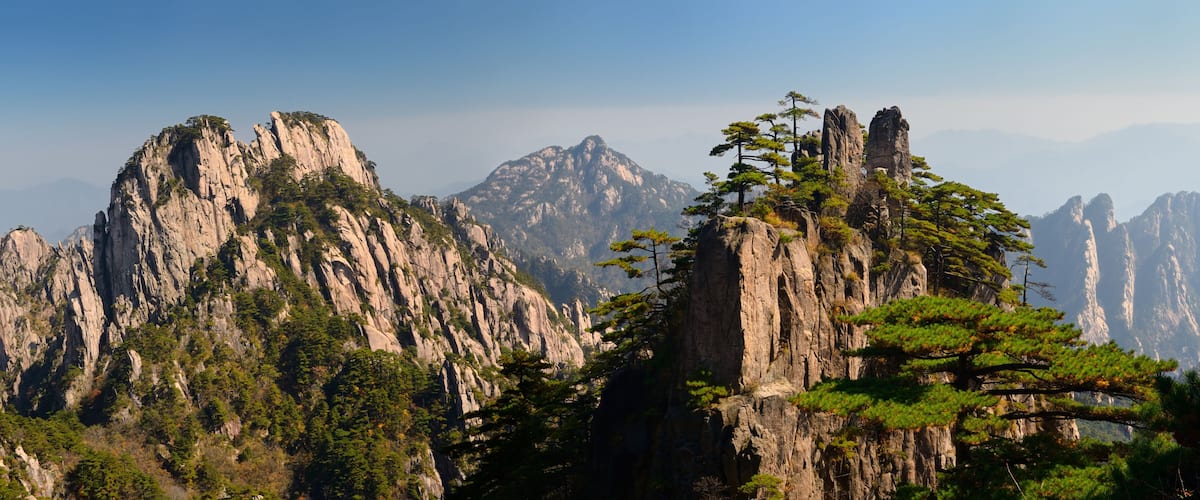 A rugged mountain range with prominent rocky peaks and scattered trees.