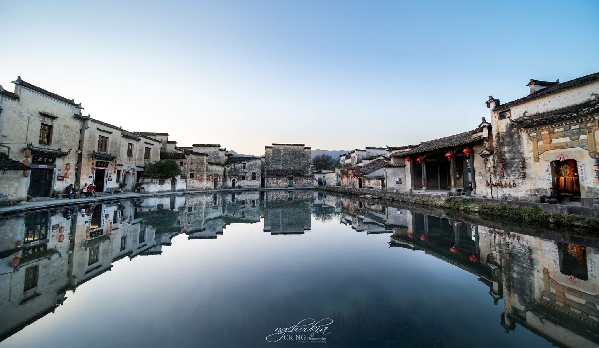 Escena apacible junto al río con arquitectura tradicional reflejada en aguas tranquilas.