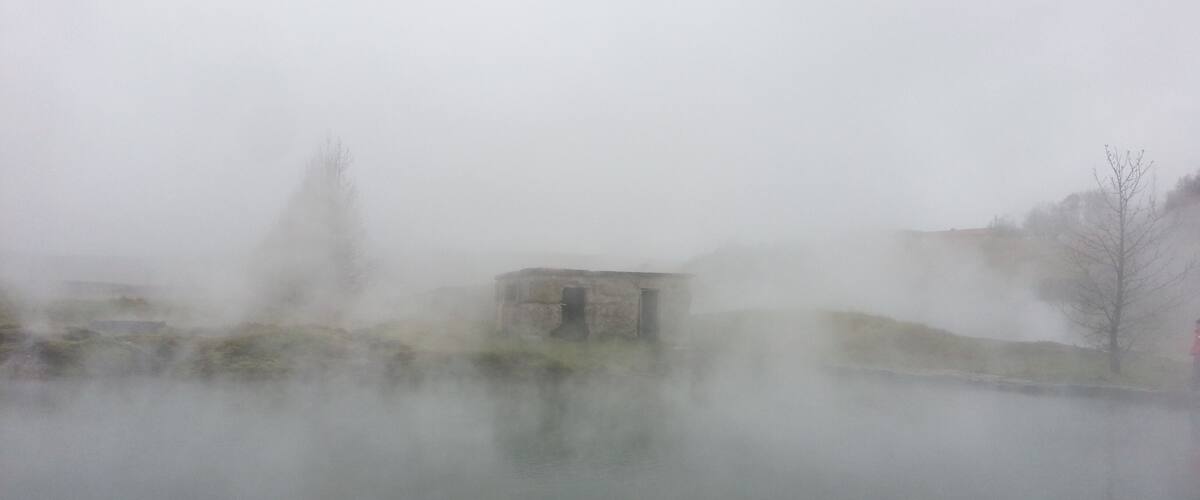 A foggy landscape with a small building near a body of water.