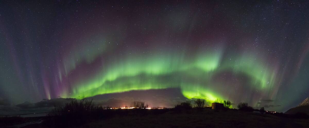 The Northern Lights over a mountainous landscape with a small settlement in the foreground.