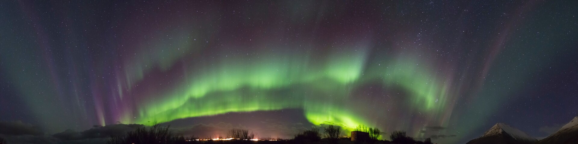 The Northern Lights over a mountainous landscape with a small settlement in the foreground.