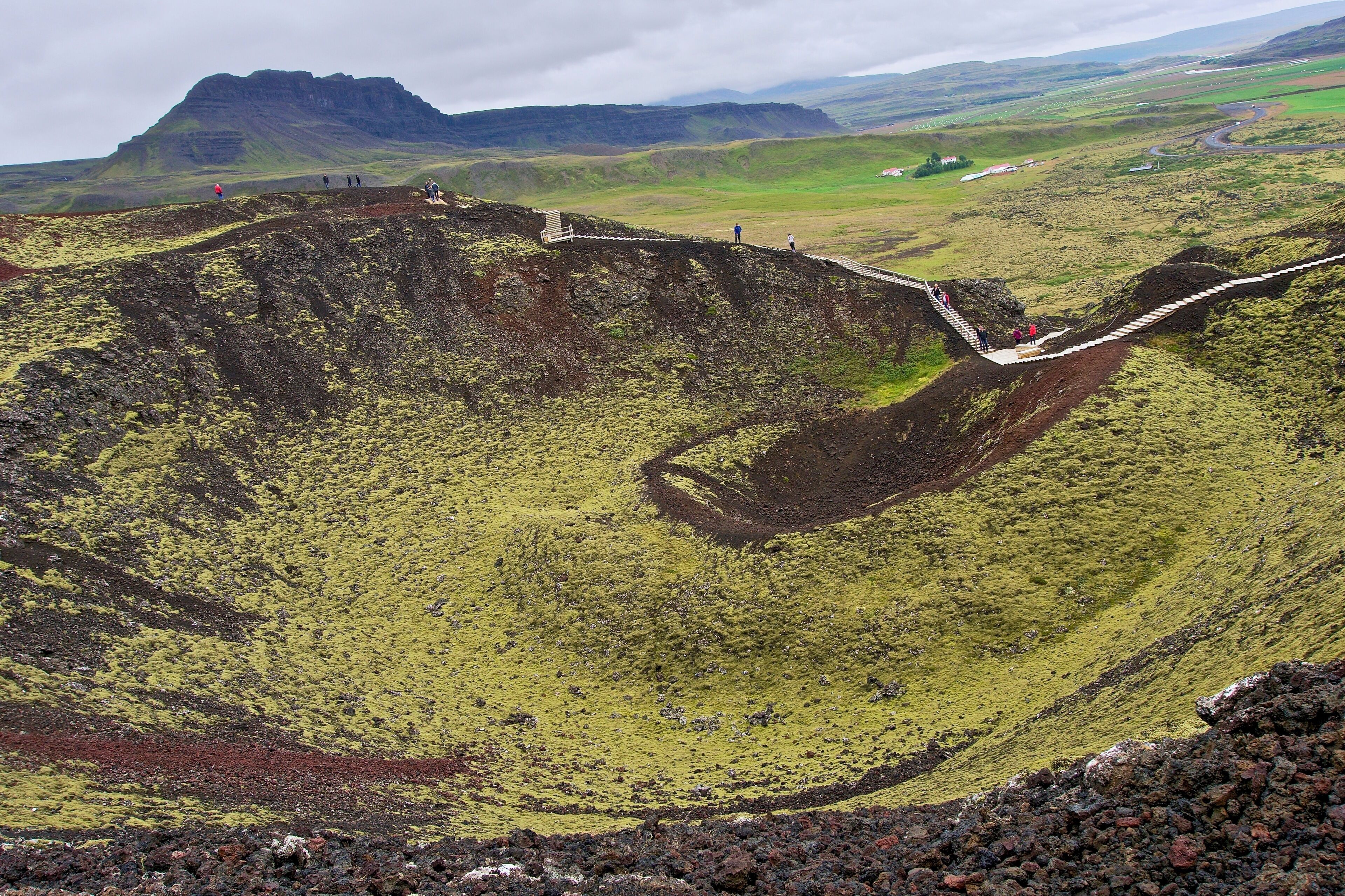 A volcanic crater with a winding road and people walking.