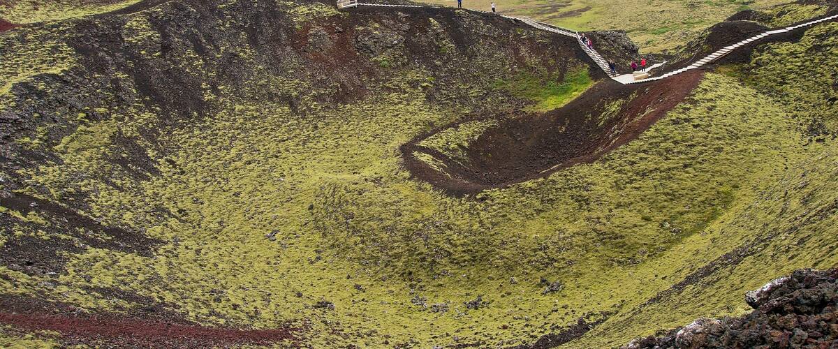 A volcanic crater with a winding road and people walking.