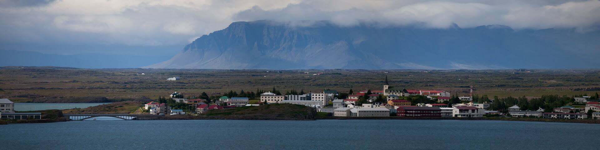 A coastal town with a prominent church, a bridge, and a large mountain in the background.