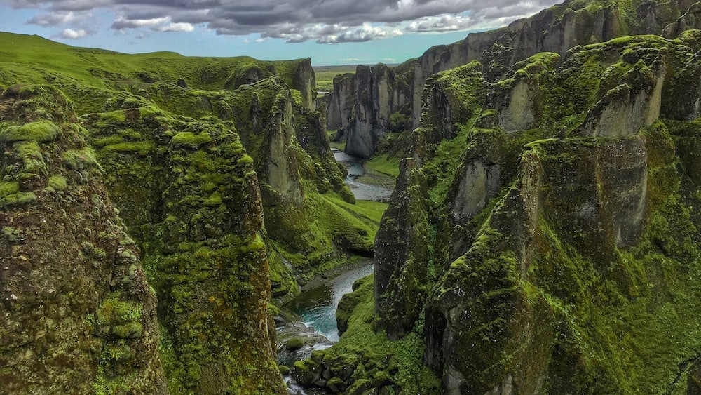 Une rivière qui traverse un canyon aux falaises verdoyantes recouvertes de mousse.