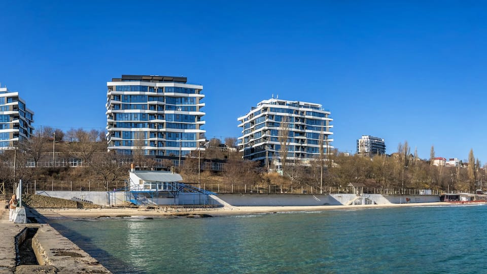 A coastal cityscape with modern high-rise buildings, a pier, and a beach.