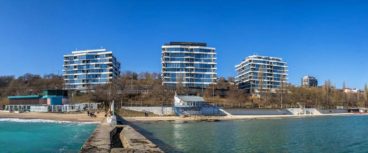 A coastal cityscape with modern high-rise buildings, a pier, and a beach.