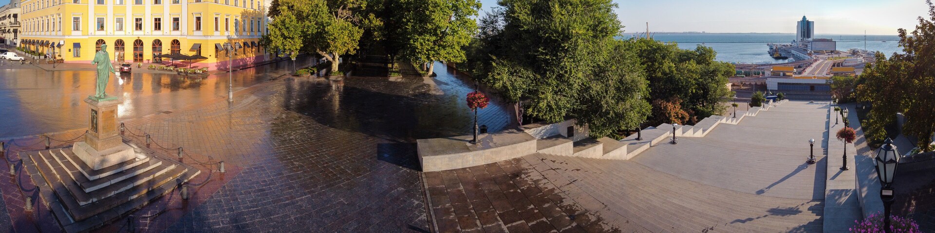 Un paseo fluvial con una estatua, árboles y una vista distante de un puente y edificios.