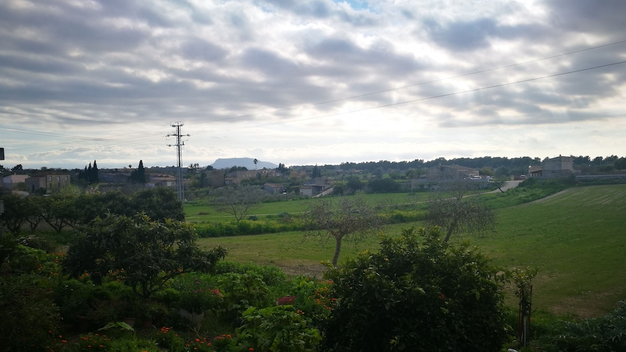 A rural landscape with green fields, scattered houses, and a cloudy sky.