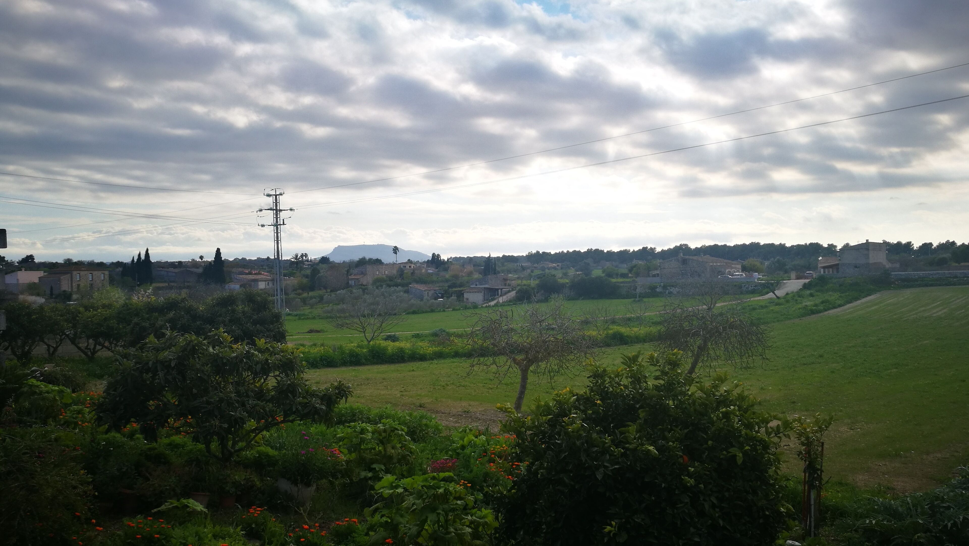 A rural landscape with green fields, scattered houses, and a cloudy sky.