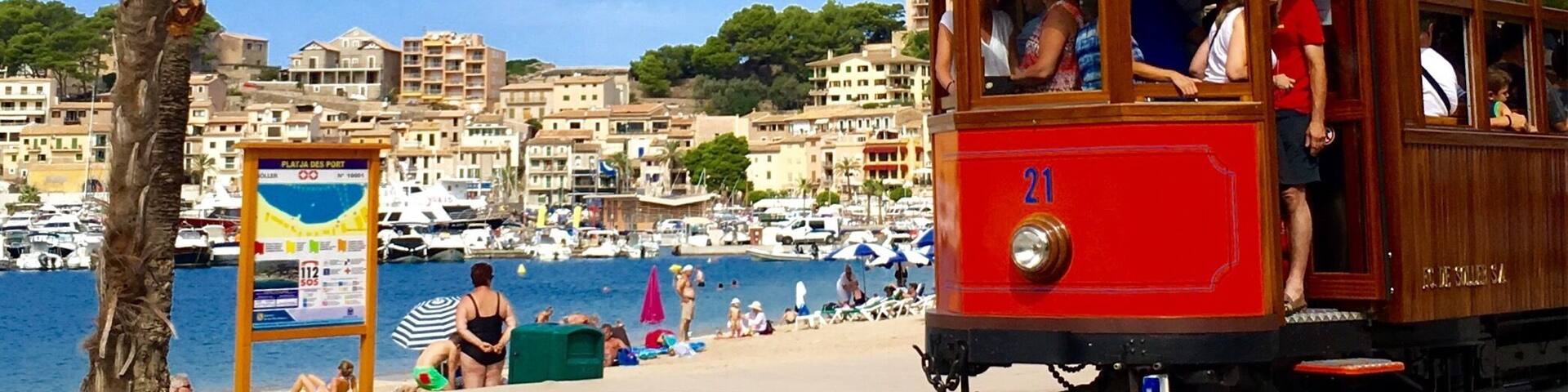 A red trolley moving along a track with a beach and marina in the background.