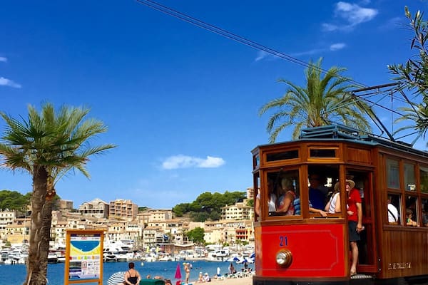 Un tramway rouge se déplace sur des rails, avec une plage et un port de plaisance en arrière-plan.