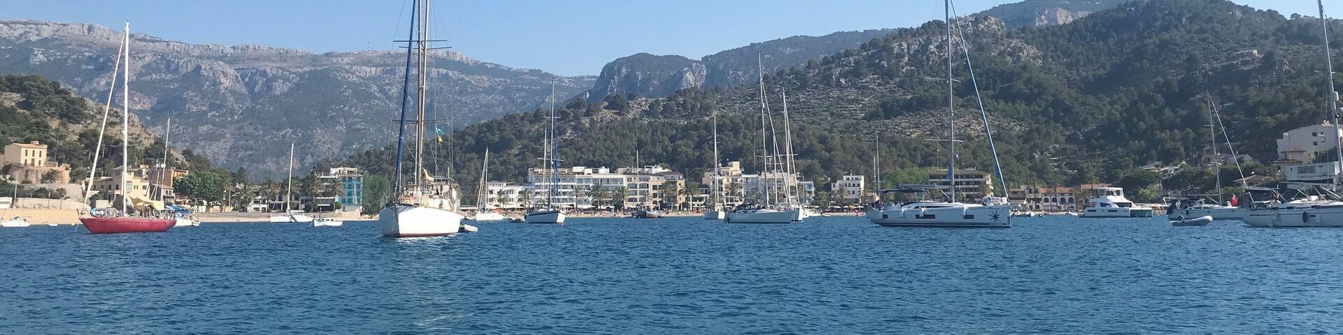 A marina with sailboats and yachts docked, a sandy beach, and a mountainous backdrop.