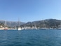 A marina with sailboats and yachts docked, a sandy beach, and a mountainous backdrop.
