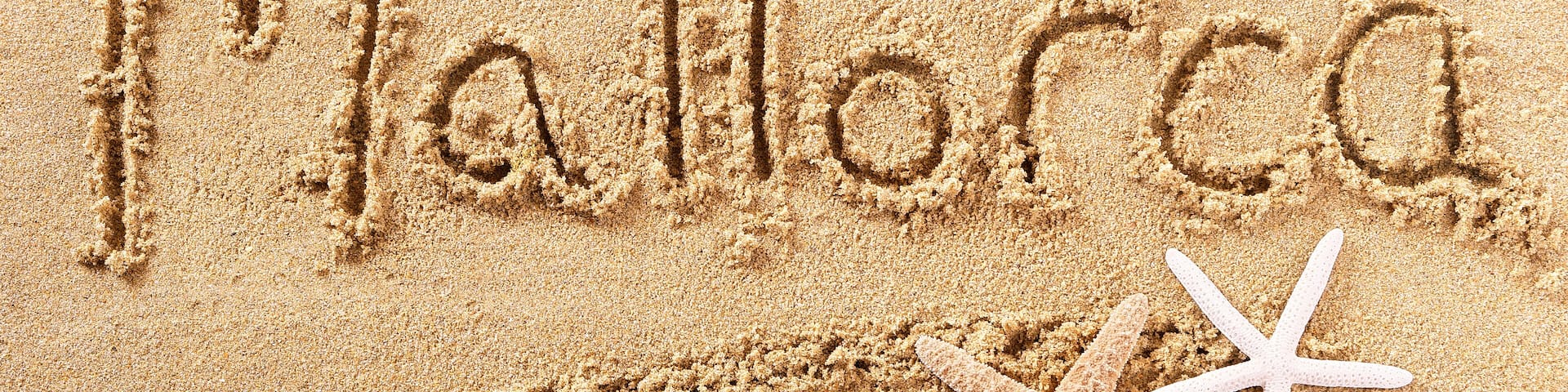 The word "Mallorca" written in sand with a starfish and a seashell nearby.