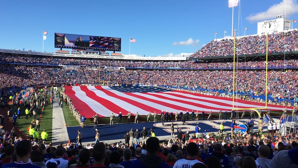 A stadium filled with spectators, an American flag, and a large screen displaying an event.