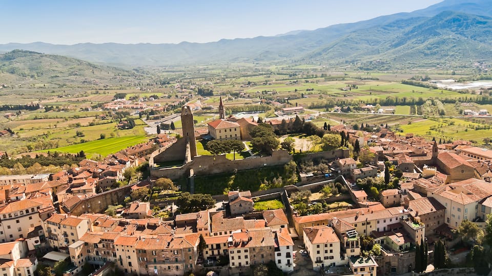 A historic town with a prominent church tower, surrounded by rolling hills and vineyards.