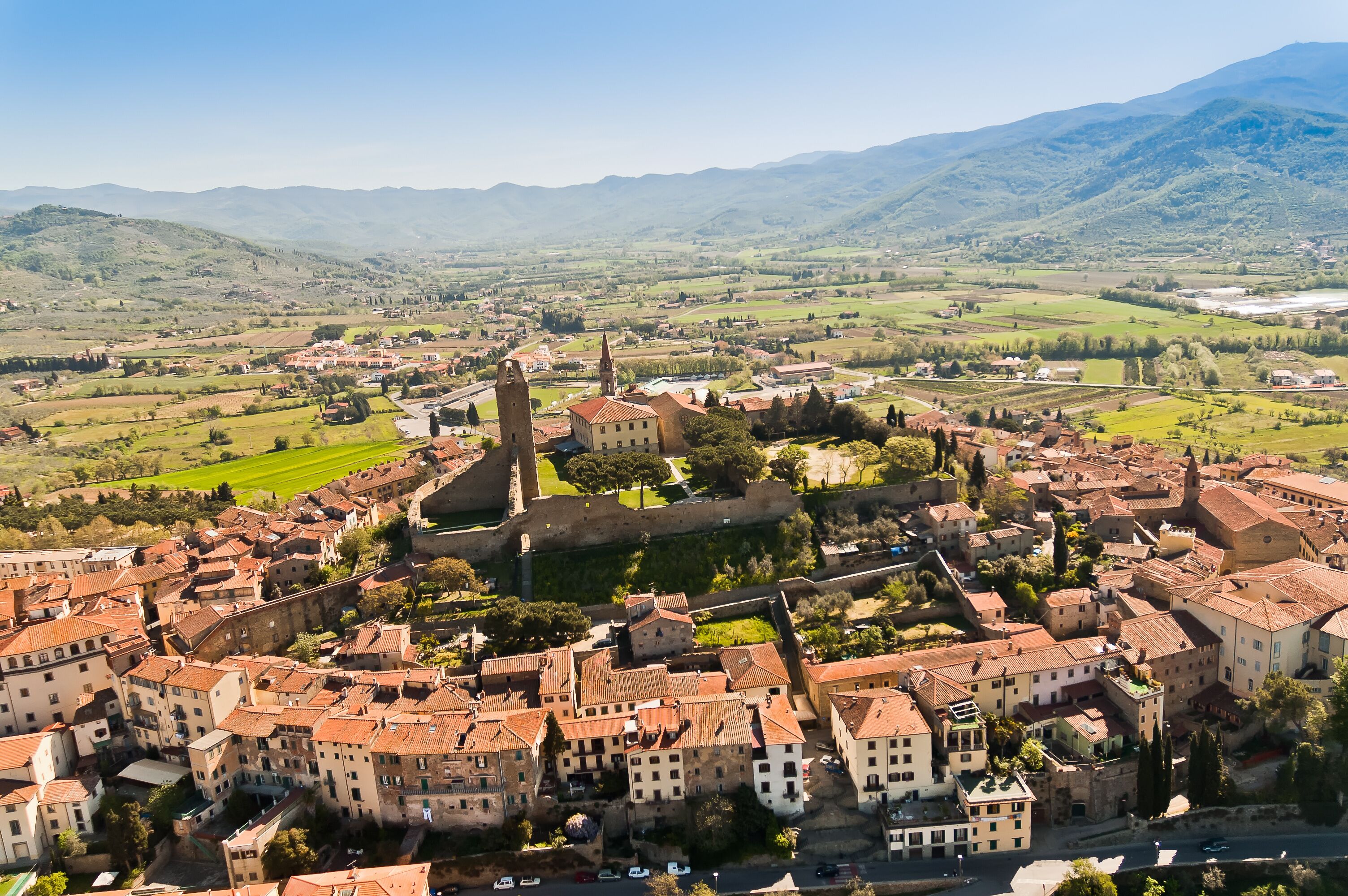 A historic town with a prominent church tower, surrounded by rolling hills and vineyards.