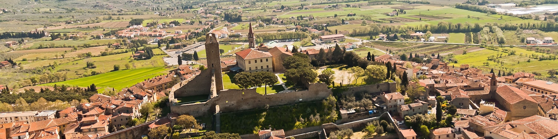 A historic town with a prominent church tower, surrounded by rolling hills and vineyards.