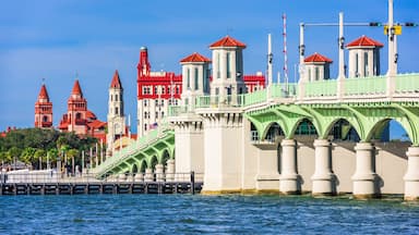 A bridge with green arches and a red building with multiple towers in the background.