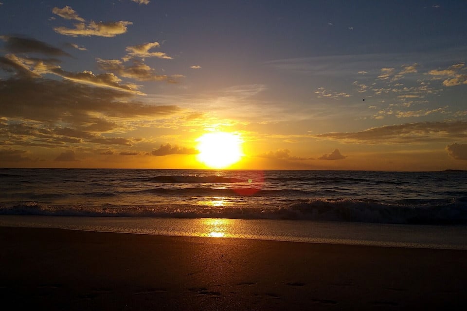 A sunset over the ocean with waves on the shore.