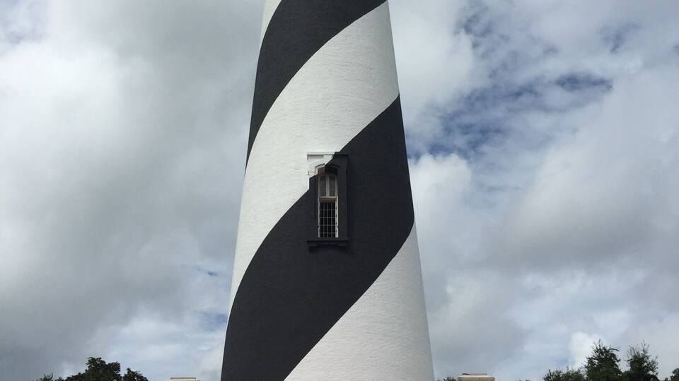 Ein Leuchtturm mit schwarz-weiß gestreiftem Muster, einem roten Dach und einem kleinen Fenster am Turm.