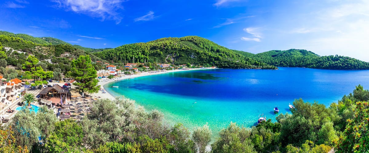 A coastal town with a turquoise bay, surrounded by lush green hills and a clear blue sky.