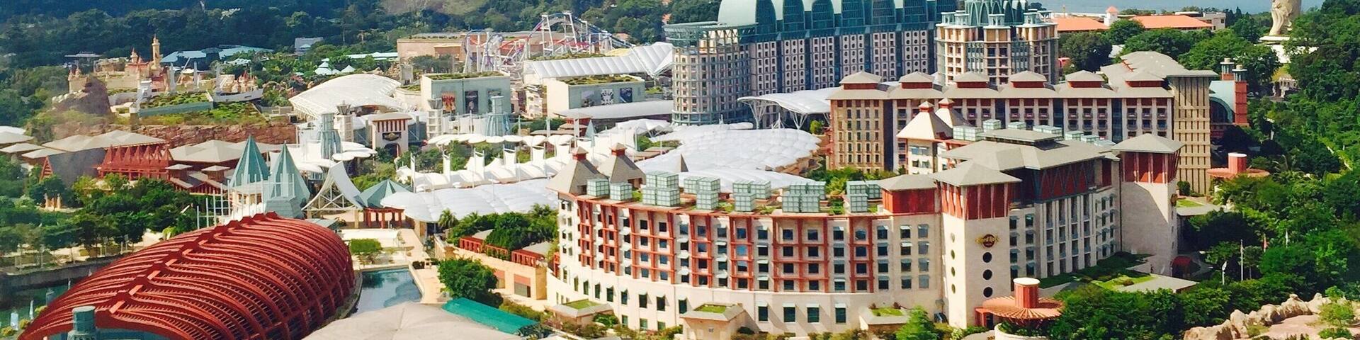 A cable car above a coastal resort with buildings, a marina, and a large dome structure.
