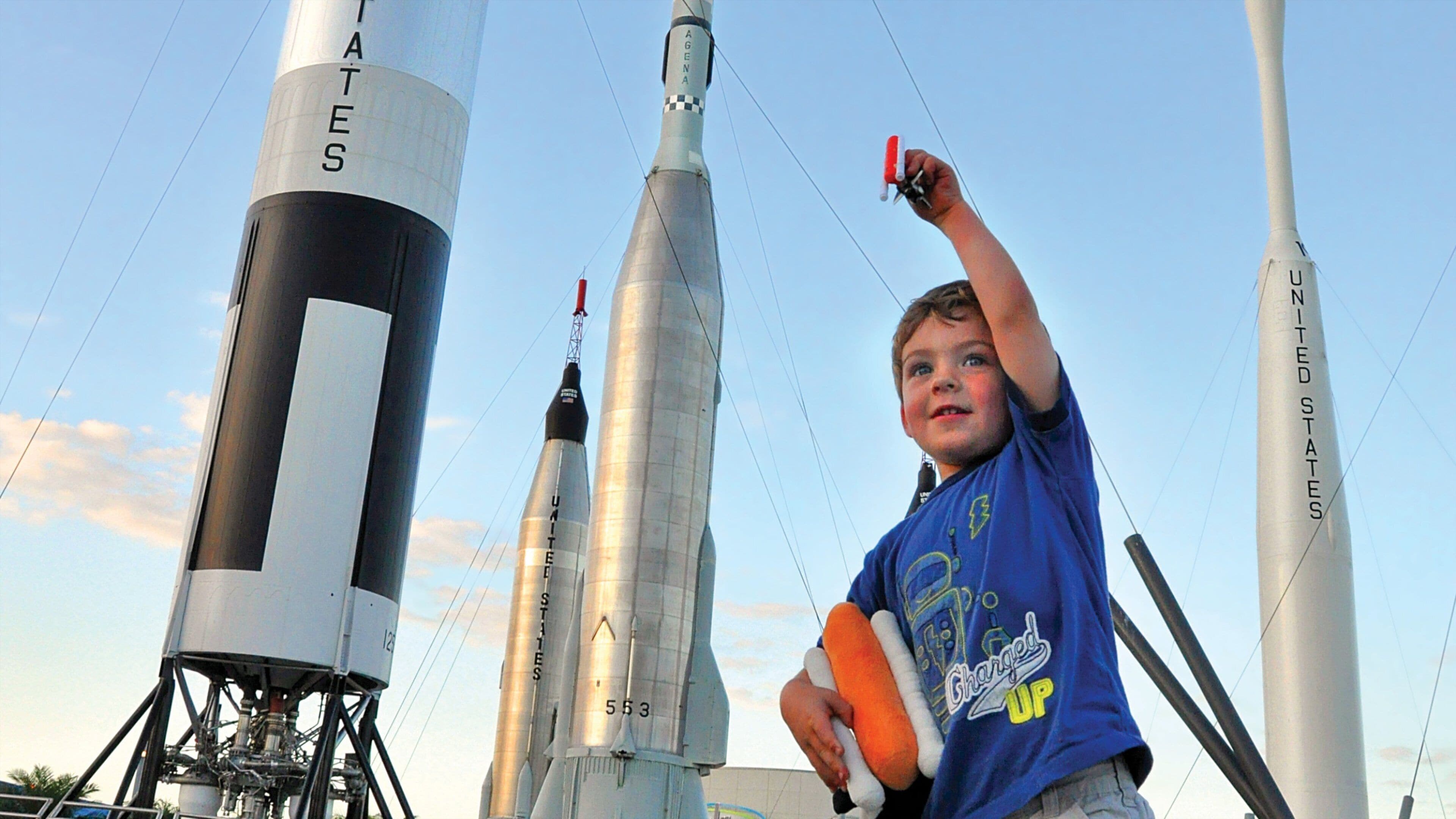 Un niño sosteniendo un cohete de juguete frente a un transbordador espacial.