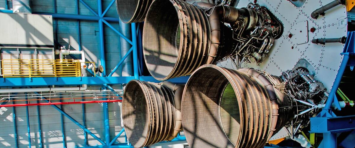 Large industrial machinery with multiple cylindrical components, blue structural supports, and a complex network of pipes and wires.