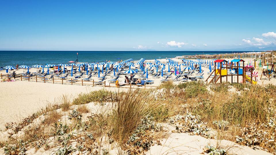 A beach with numerous blue and white striped umbrellas, sun loungers, and a lifeguard tower.