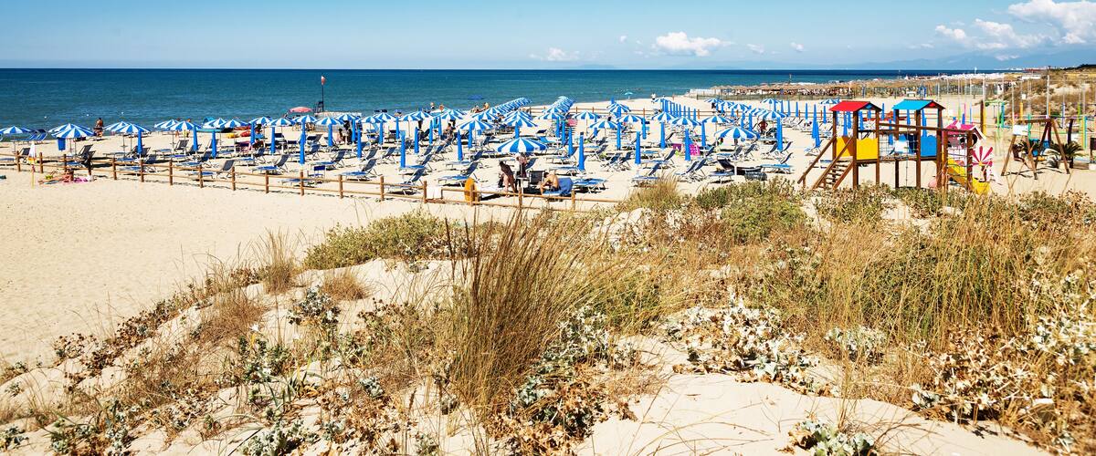 A beach with numerous blue and white striped umbrellas, sun loungers, and a lifeguard tower.