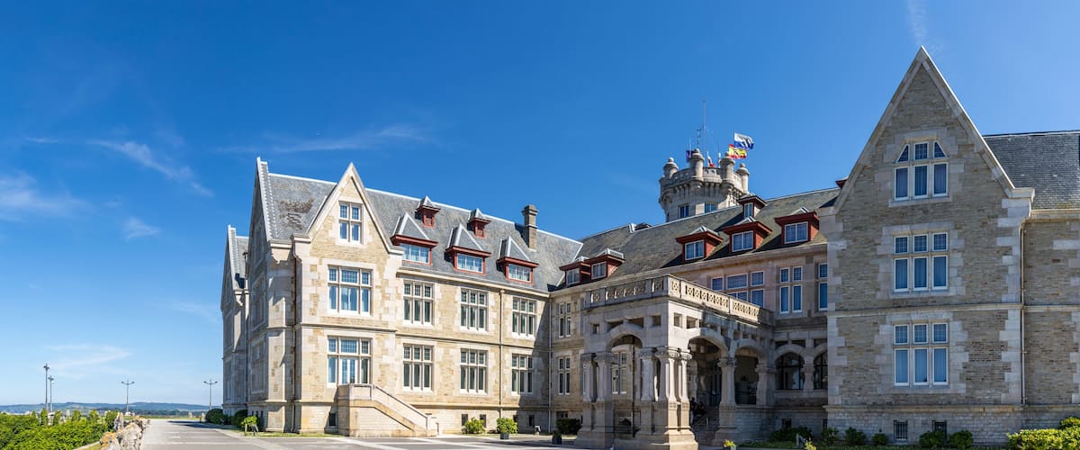 A historic stone building with multiple towers and a coastal view.