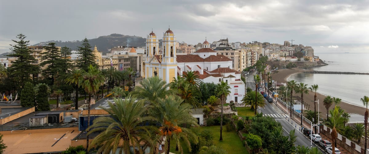 A coastal cityscape with a prominent church, palm trees, and a beach.