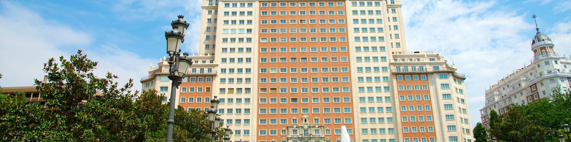 Un edificio grande de varios pisos con una fuente central y follaje circundante.
