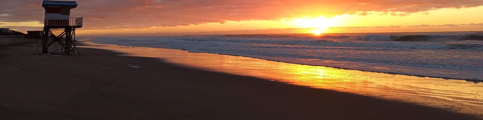 A beach with a lifeguard tower at sunset.