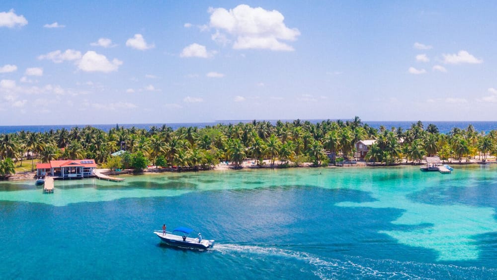 A tropical island with clear turquoise waters, a boat, and a thatched-roof structure.
