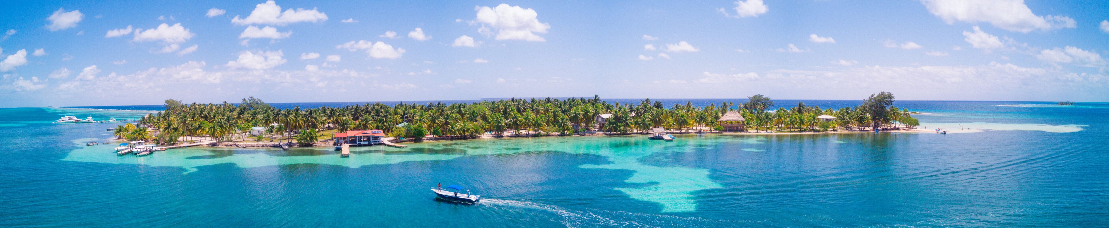 A tropical island with clear turquoise waters, a boat, and a thatched-roof structure.