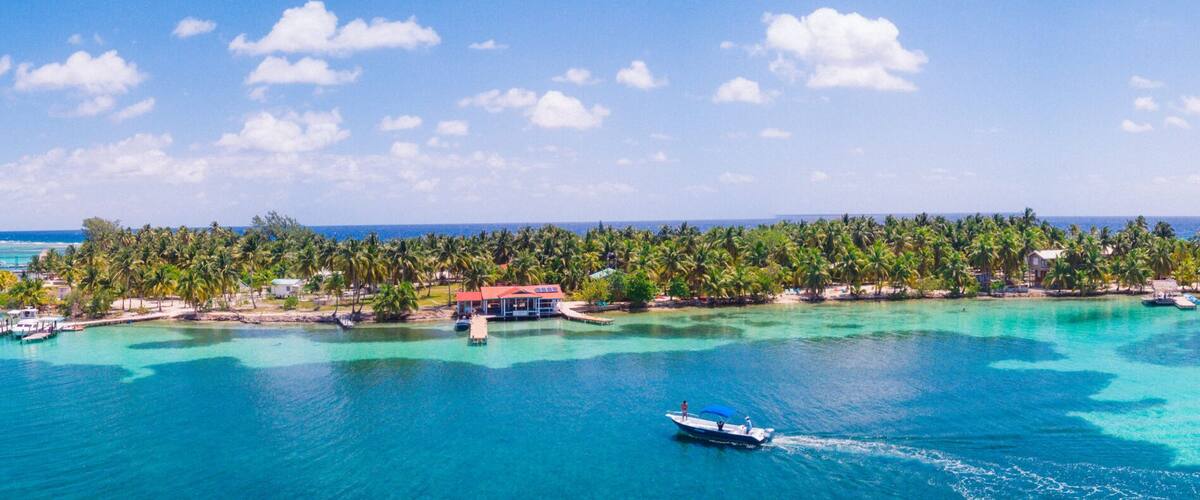 A tropical island with clear turquoise waters, a boat, and a thatched-roof structure.