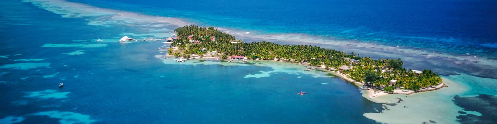 An aerial view of a tropical island with clear turquoise waters, a small beach, and dense palm tree vegetation.