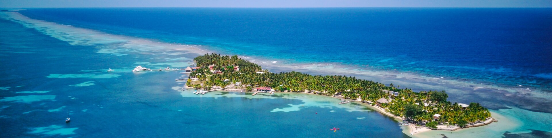 Vista aérea de una isla tropical con aguas turquesas cristalinas, una pequeña playa y densa vegetación de palmeras.