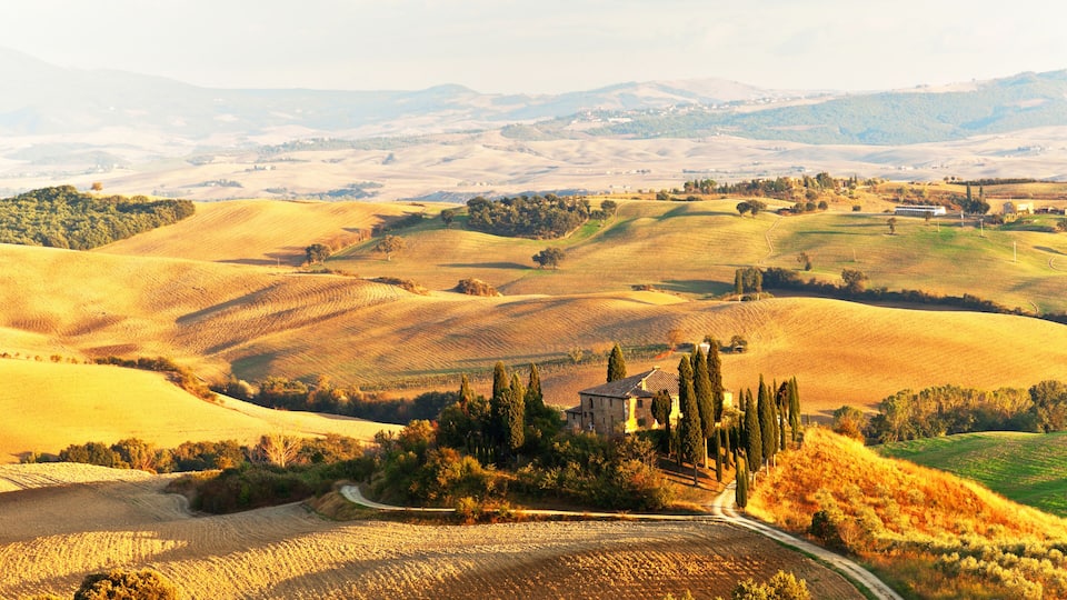 Rolling hills, a winding road, and a historic building surrounded by trees.