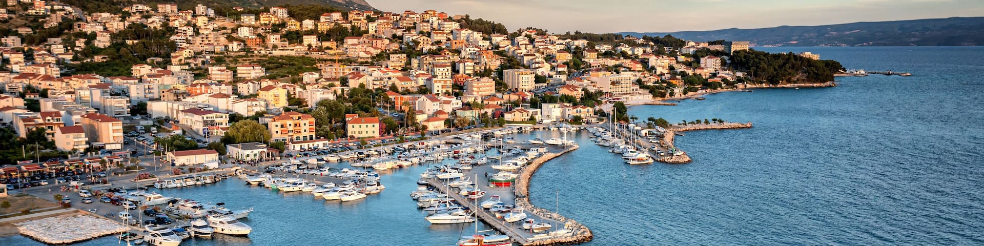 A coastal town with a marina filled with boats, surrounded by hills and a clear sky.